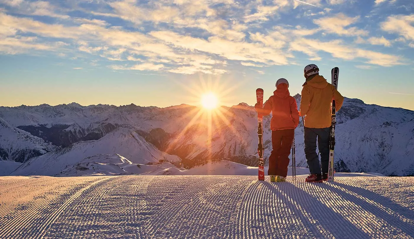 Zwei Wintersportler vor verschneiten Bergen im Abendlicht